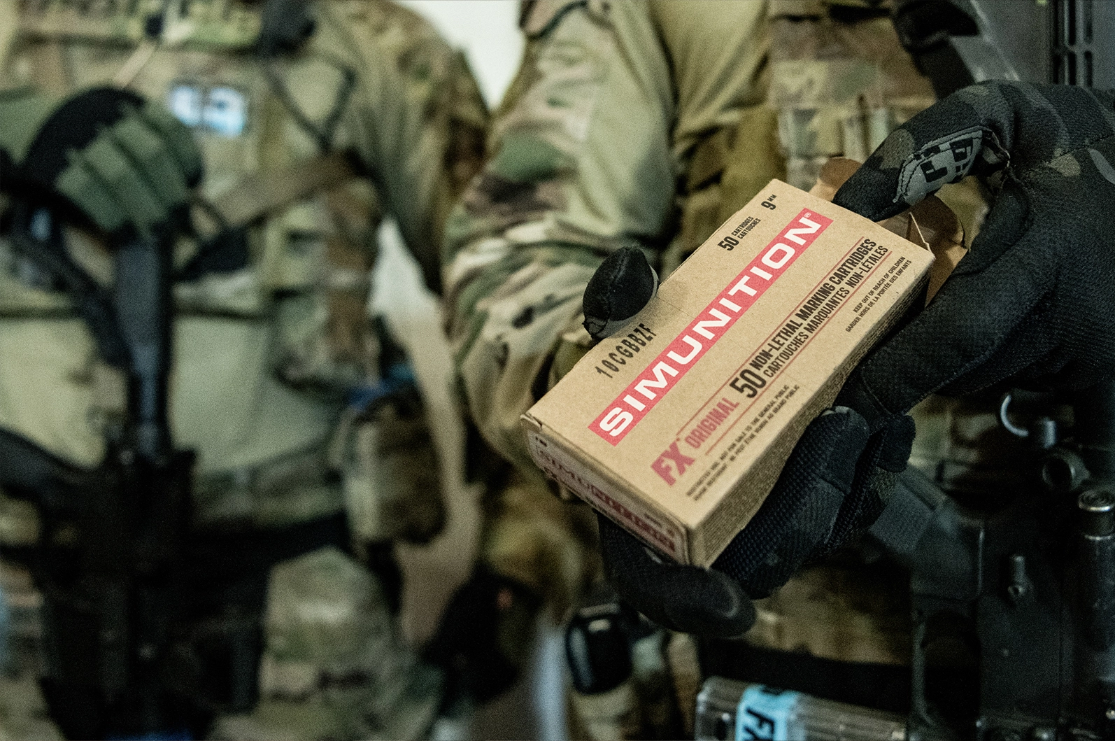 Military personnel hold a box of non-lethal marking cartridges